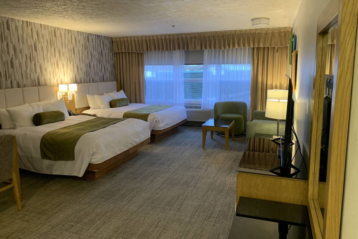 A hotel room with two beds, a desk, a chair, a TV, and a window with curtains.