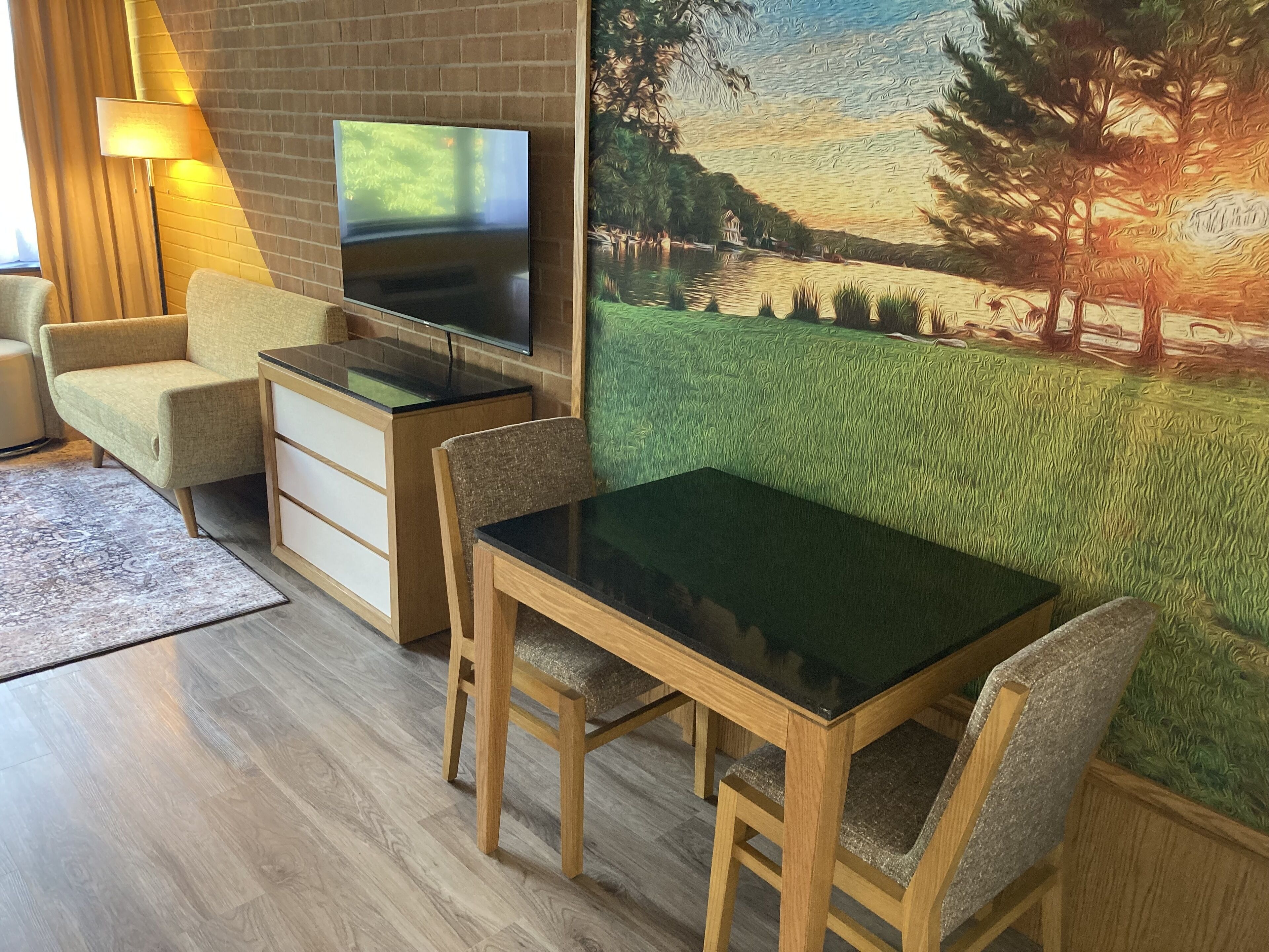 Ett modernt vardagsrum med en platt-TV som är monterad på en tegelvägg, ett matbord i tr ä med stolar, en soffa och en mönstrad matta.