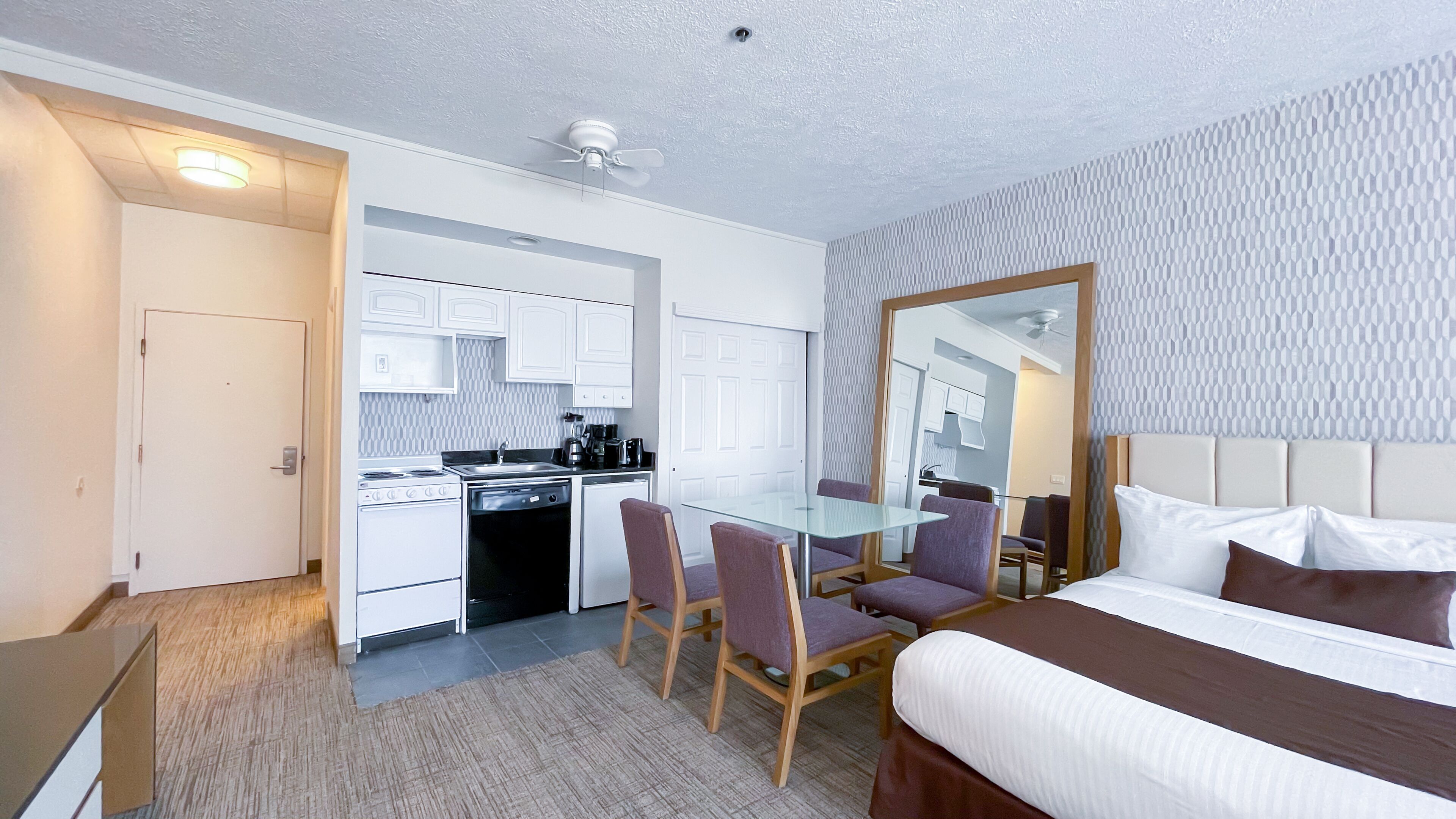 Une chambre d’hôtel comprenant un lit, une table à manger en verre avec des chaises, un coin cuisine et une salle de bain.