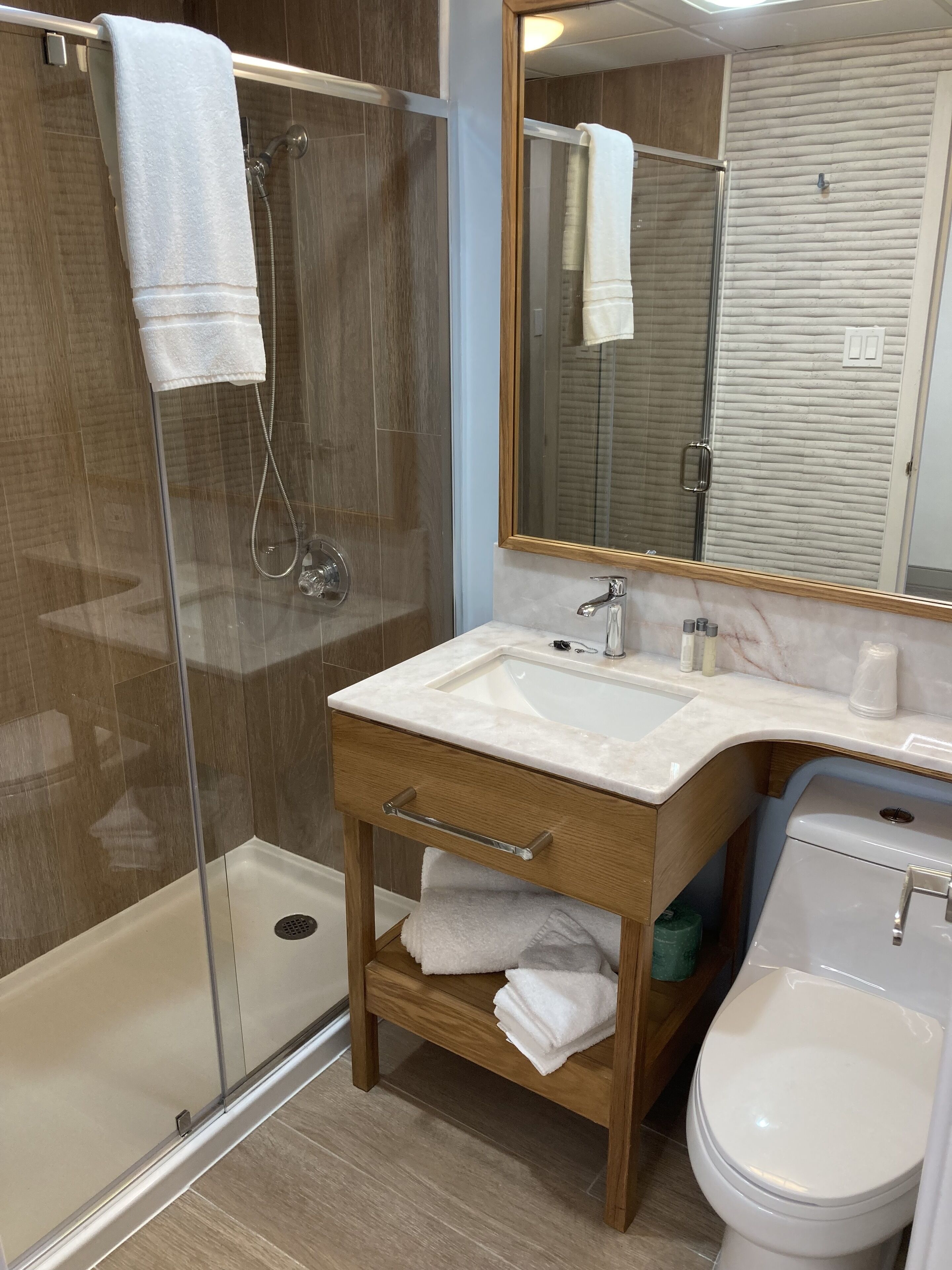 Un baño moderno con ducha de vidrio, tocador de madera con lavamanos y un inodoro.