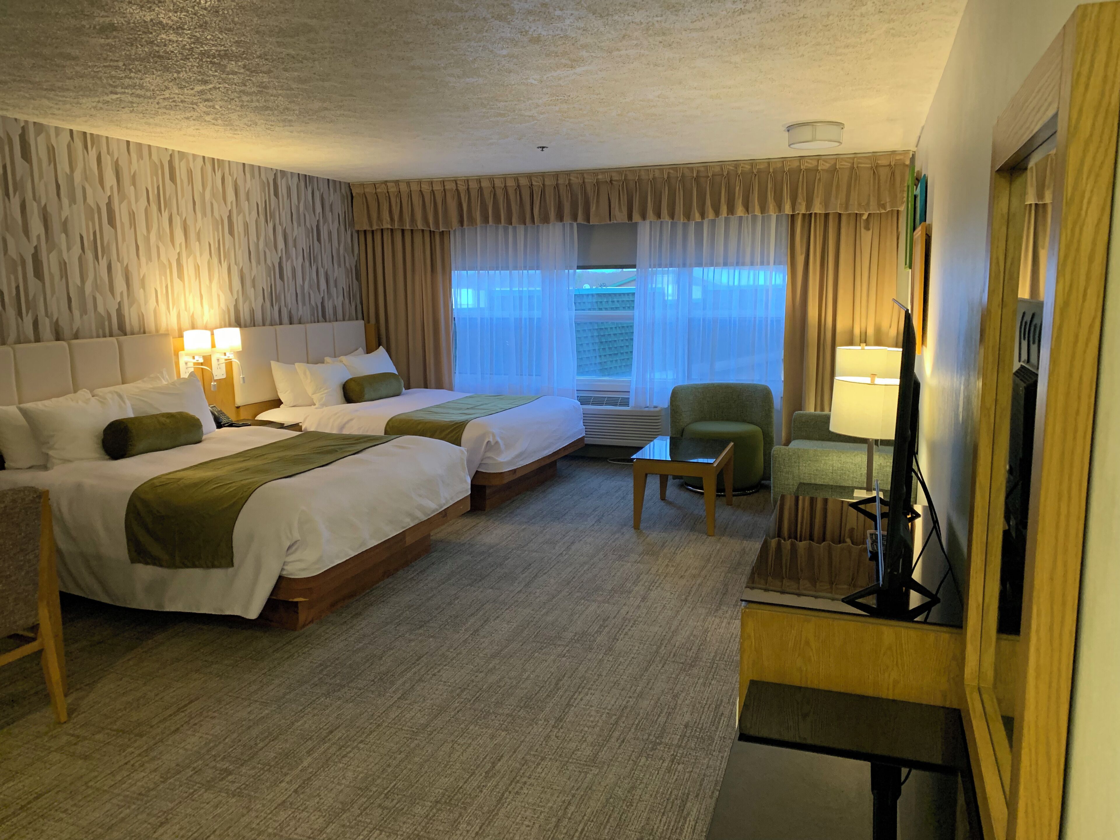 Une chambre d’hôtel avec deux lits, un bureau, une chaise, une télévision et une fenêtre avec des rideaux.