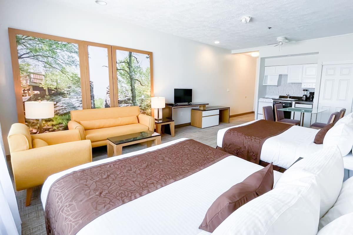 A hotel room with two beds, a sofa, a desk, a TV, and a kitchenette.