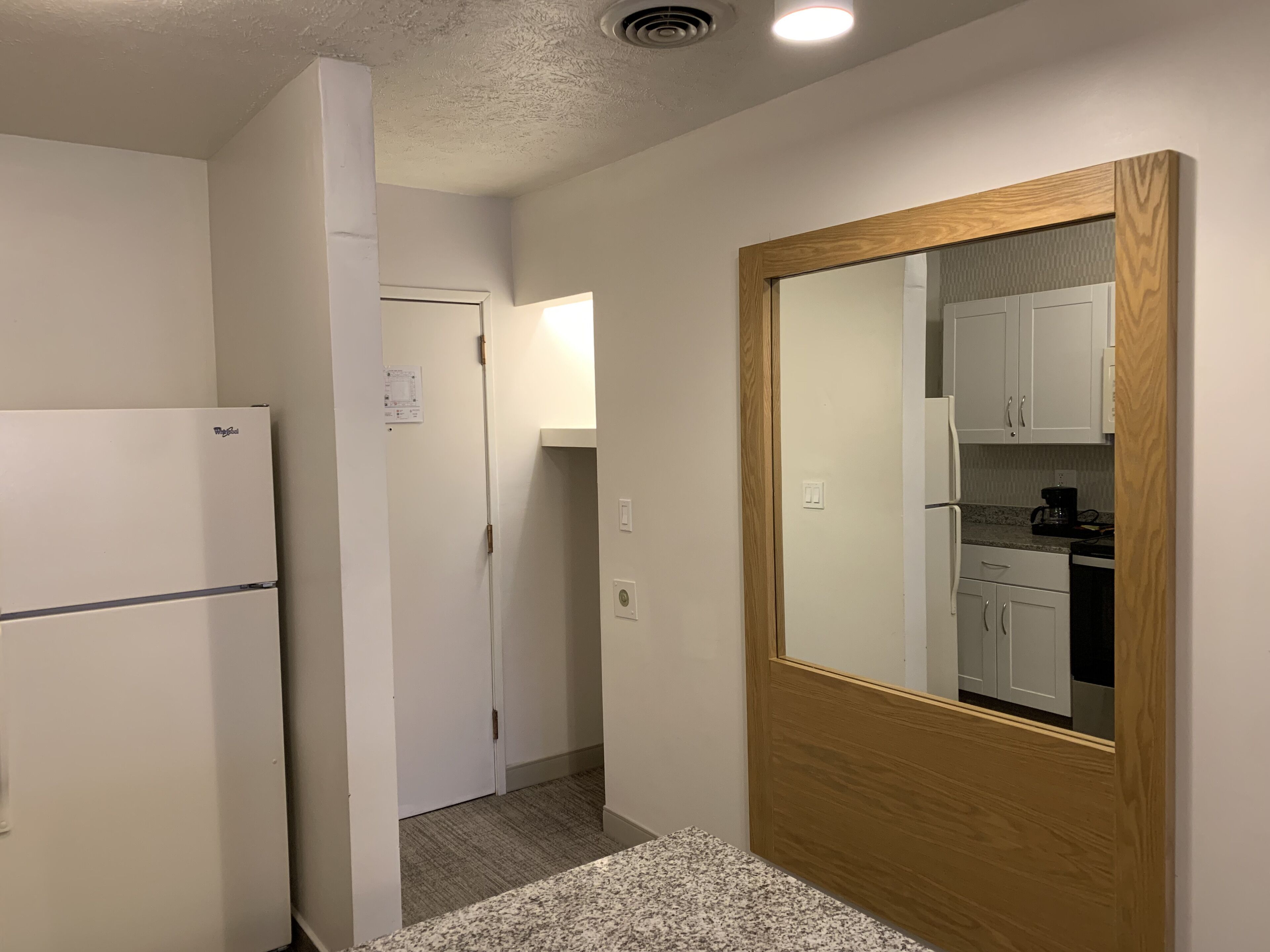 Eine kleine Küche mit einem Kühlschrank, einer Holztür und einer Arbeitsplatte mit einer Kaffeemaschine.