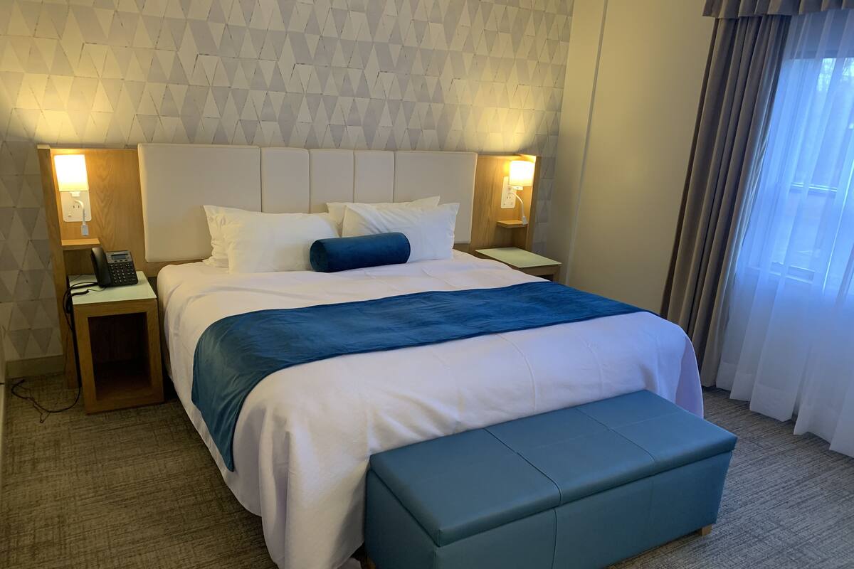 A hotel room with a large bed, bedside tables with lamps, a telephone, and a window with curtains.