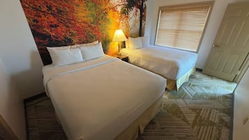 Une chambre d’hôtel avec deux lits, une table de chevet avec une lampe, une grande fresque murale sur le thème de l’automne et une moquette à motifs.