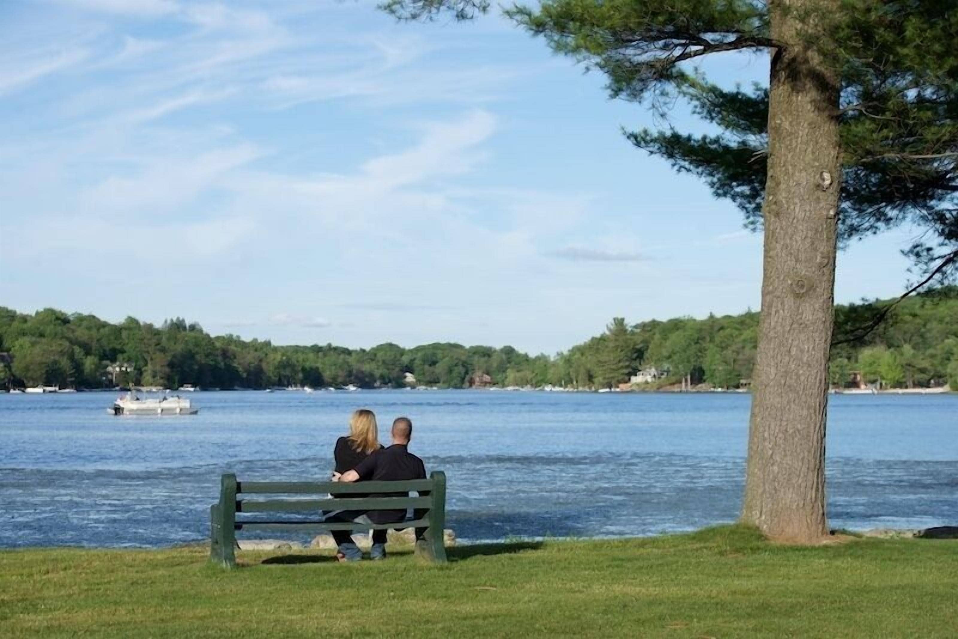 Una pareja sentada en un banco junto a un lago, con un bote al fondo.