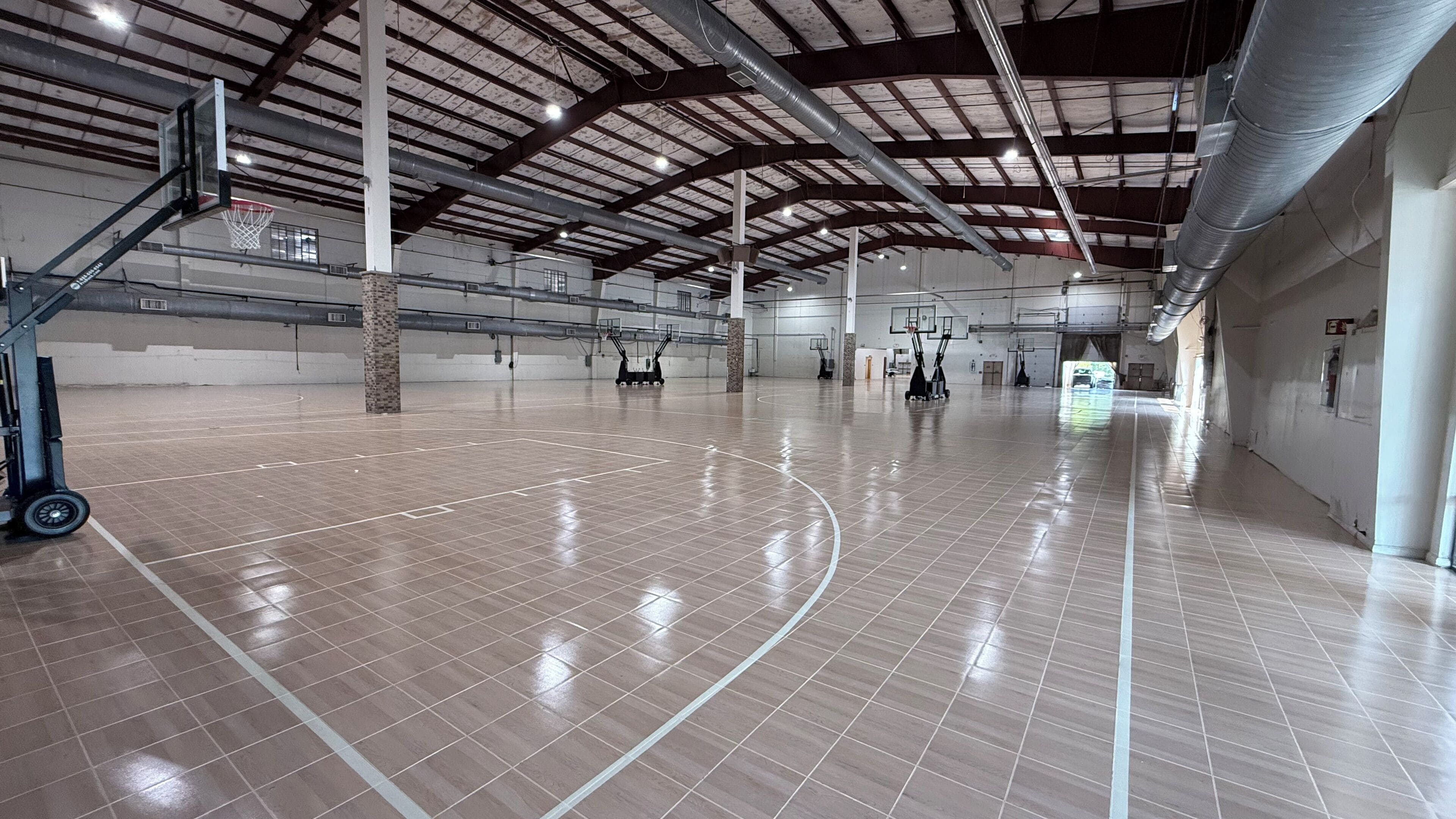 A spacious indoor basketball court with multiple hoops, a high ceiling with visible beams, and a clean, polished floor.