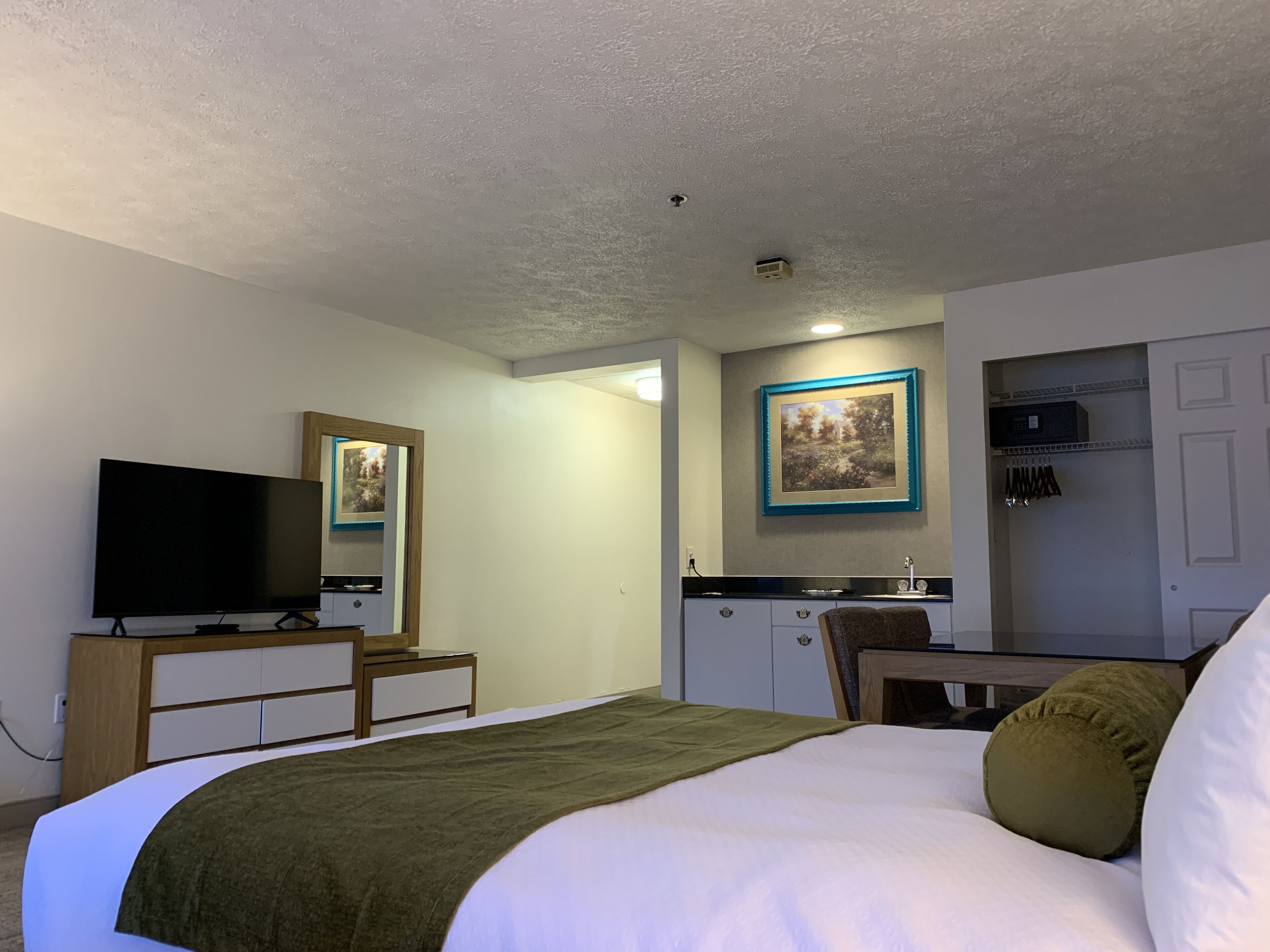 A hotel room with a bed, a television, a desk, a mirror, a picture on the wall, and a wardrobe.