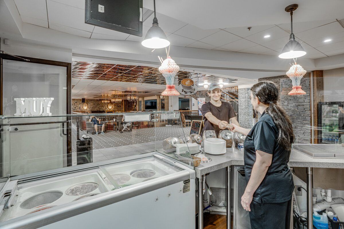 A modern kitchen area with stainless steel appliances, a large ice cream display, and hanging pendant lights.