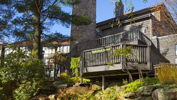 A rustic building with a wooden deck and a stone staircase leading to a pond.