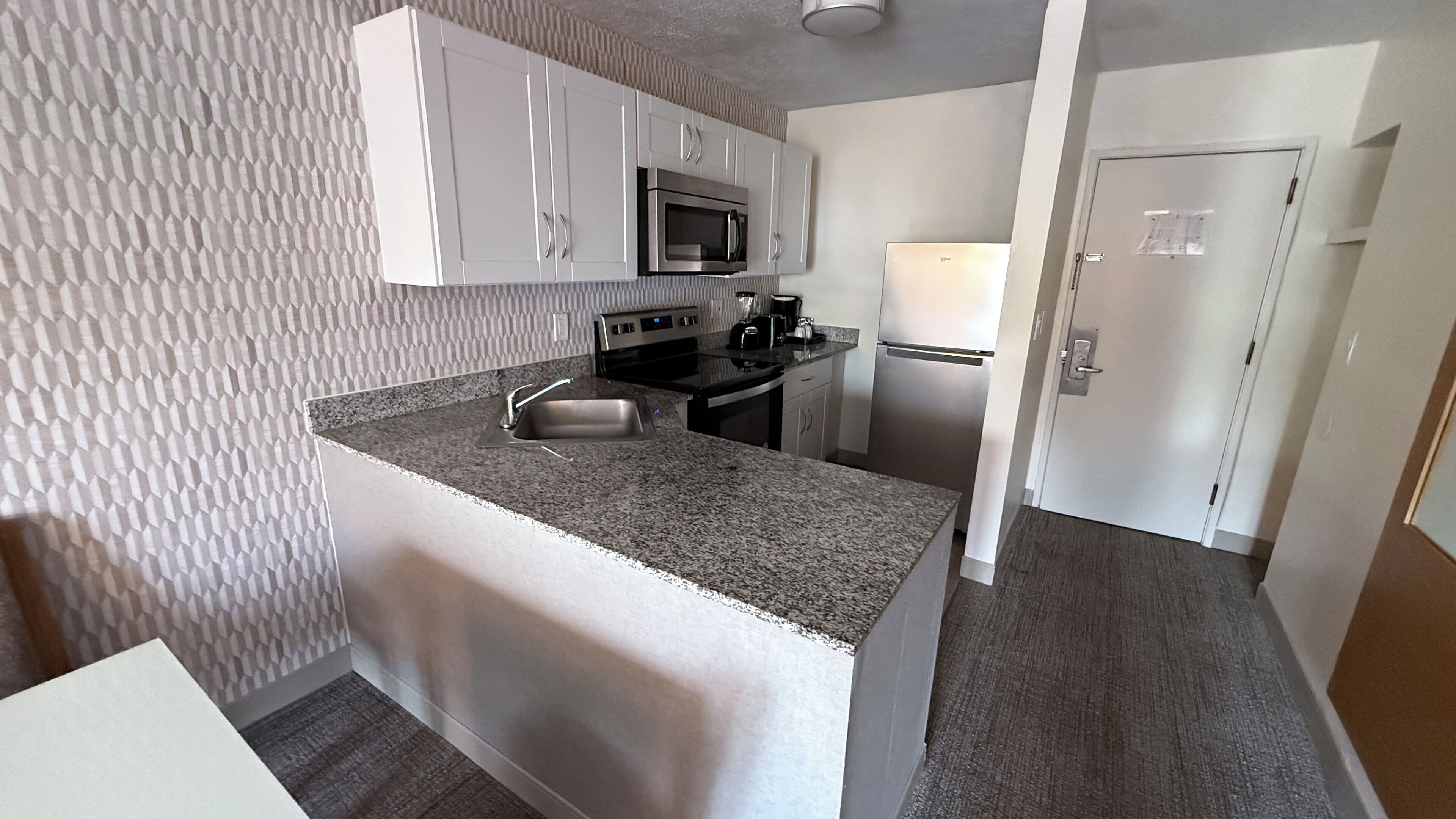 A compact kitchen with white cabinets, a stainless steel microwave, a stove, and a refrigerator.