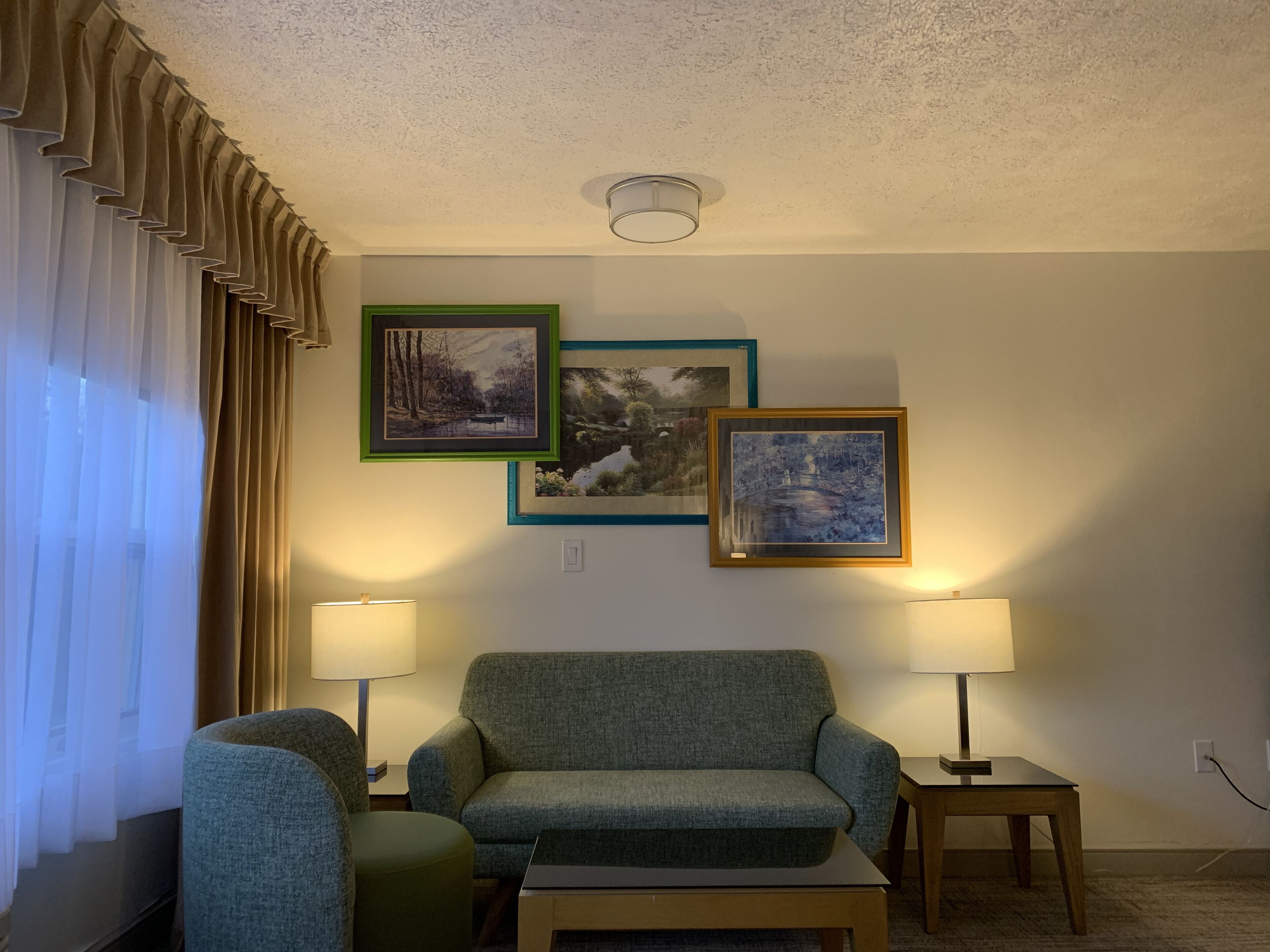 A living room with a green sofa, two side tables with lamps, and three framed pictures on the wall.