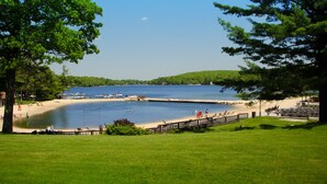 A lakeside park with picnic tables, a wooden deck, and boats on the water.