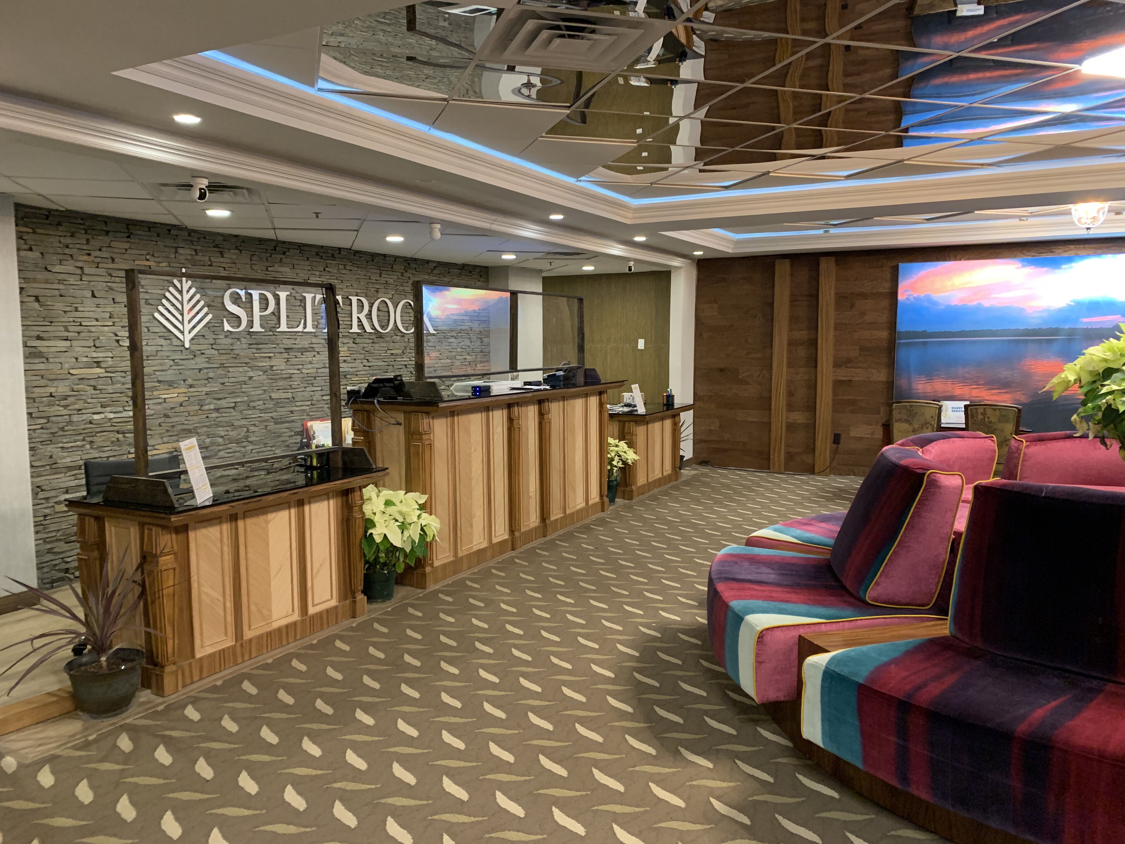 A reception area with a stone wall, a reception desk, a large window with a sunset view, and a colorful sofa.
