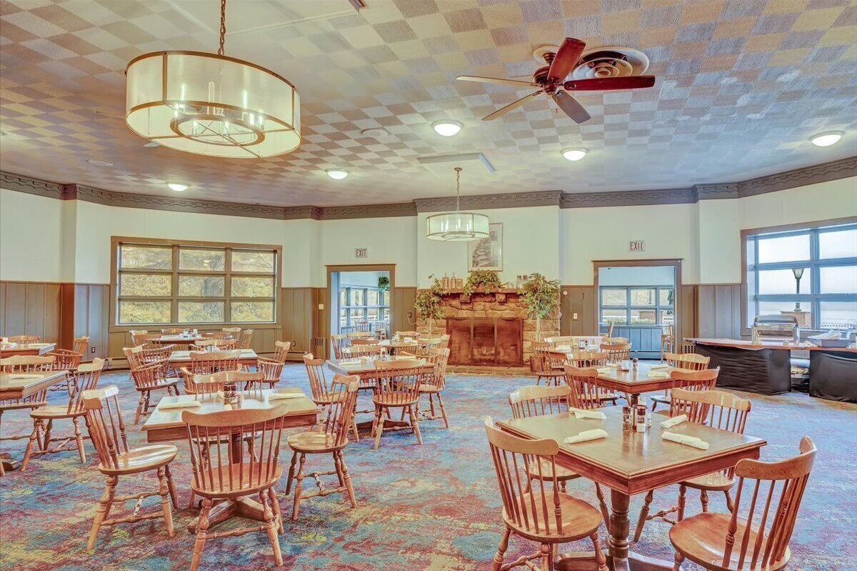 A spacious dining area with wooden tables and chairs, large windows, and a fireplace.