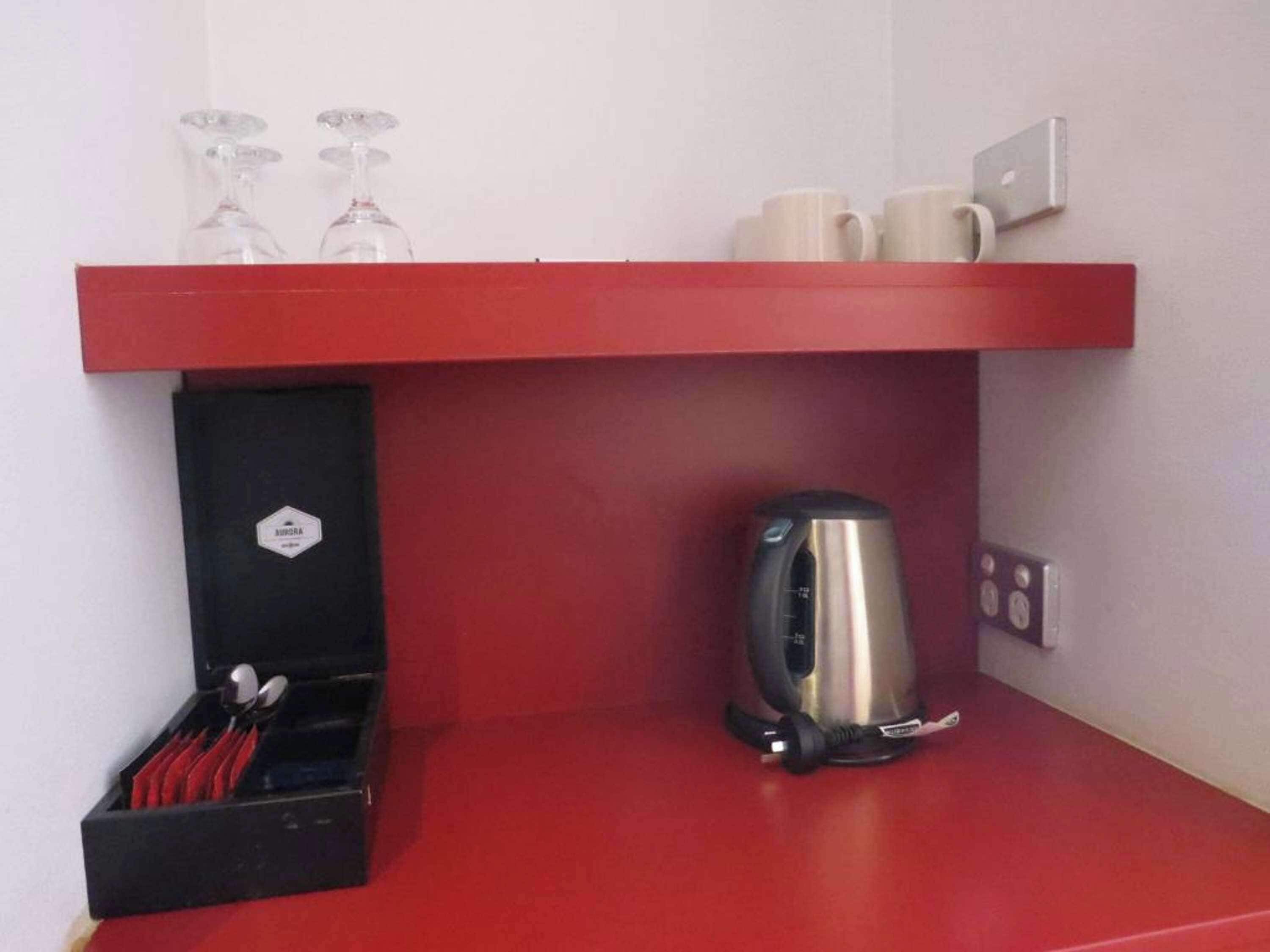 Una estantería roja con dos vasos, tres tazas, un hervidor y una caja negra con utensilios.