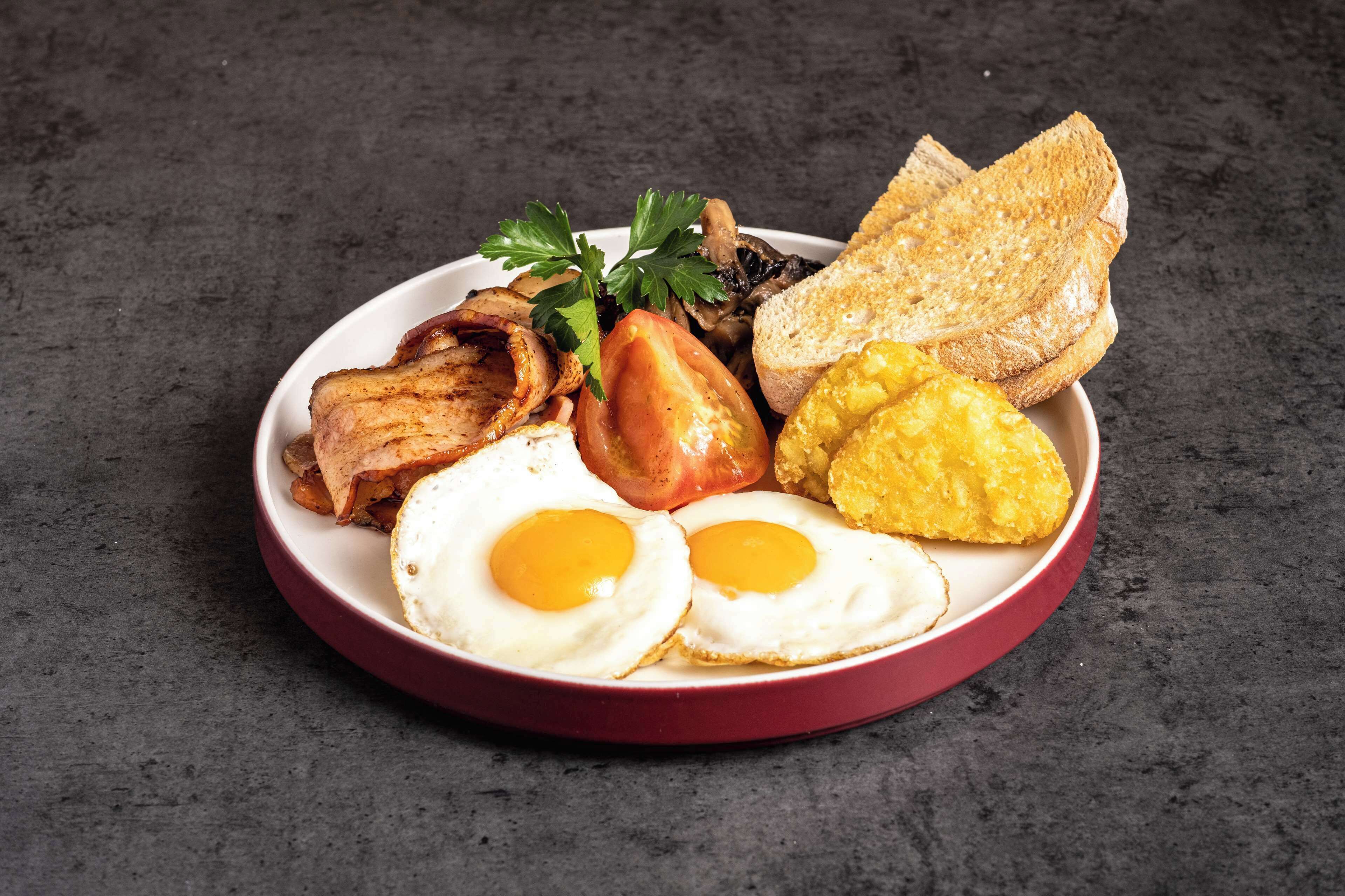 Un plato con huevos, tocino, tomates, champiñones y tostadas.