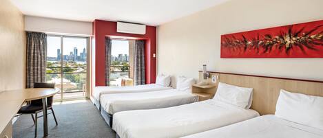 A hotel room with three beds, a desk, a chair, and a large window with a city view.