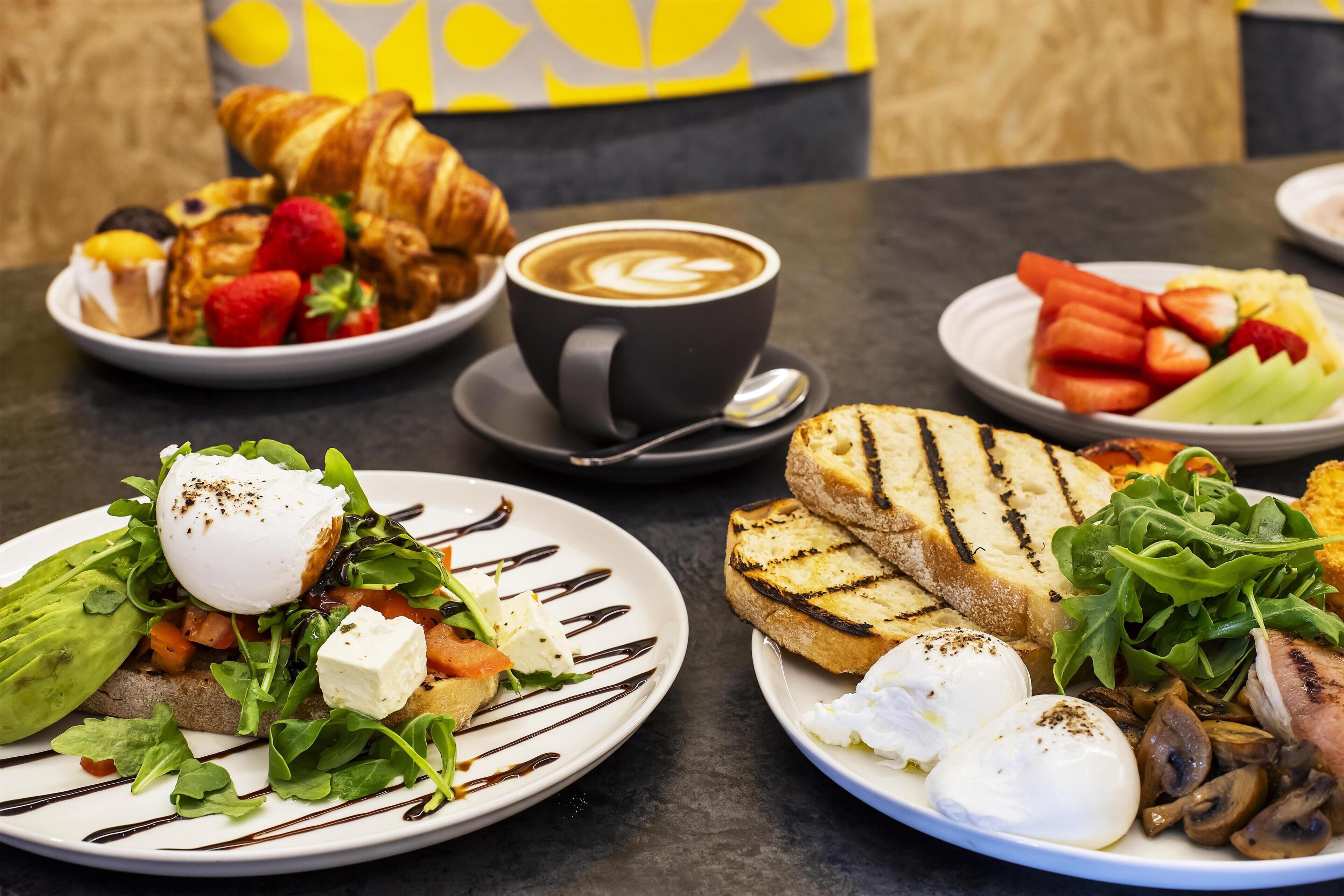 Un desayuno con croissants, café y diferentes platos que incluyen huevos, champiñones y verduras.