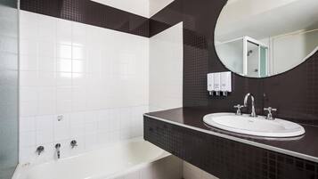 A modern bathroom with a white bathtub, a sink with two faucets, a mirror, and a dark tiled wall.