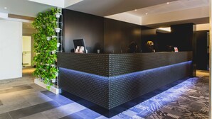 A reception desk with a patterned design, a vertical plant wall, and a patterned floor. - Metro Hotel Perth (South Perth)