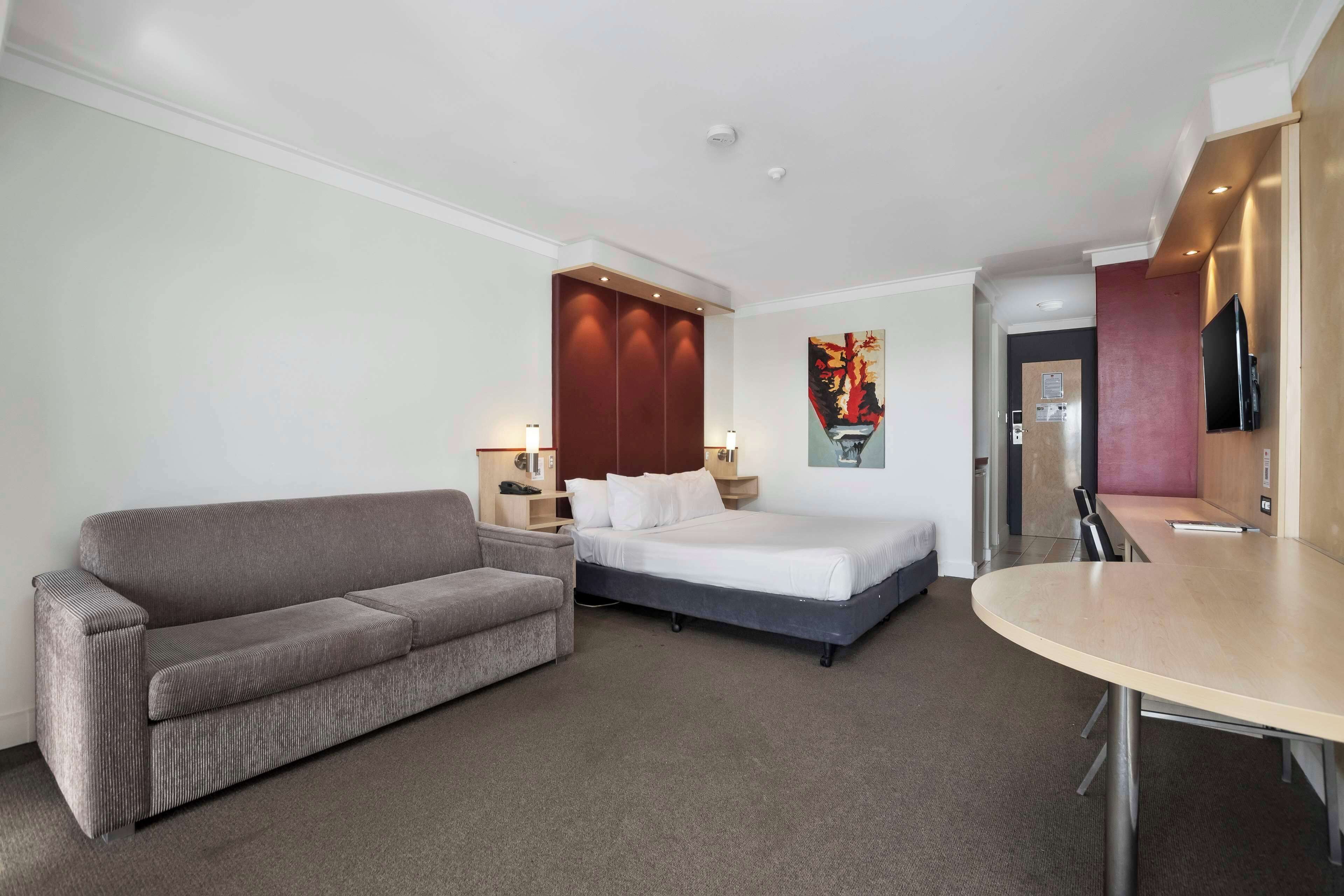 A hotel room with a bed, a sofa, a dining table, and a TV.