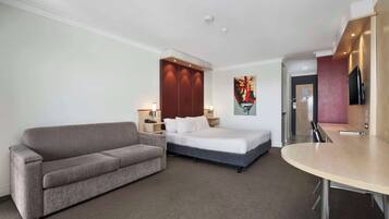 A hotel room with a bed, a sofa, a dining table, and a TV.