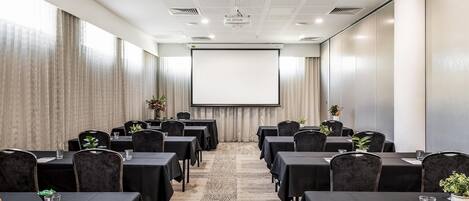 A conference room with tables, chairs, a projector screen, and a large window.