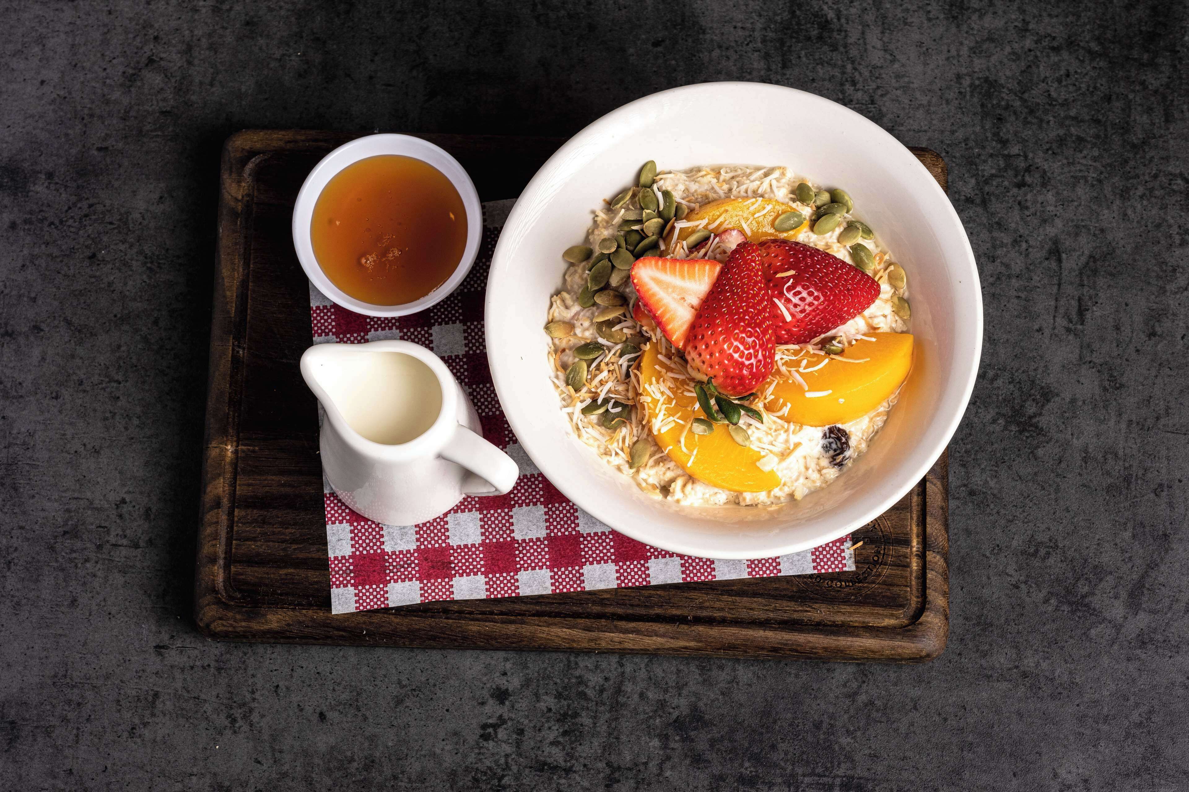 Un plateau de petit-déjeuner avec du porridge, des fruits, une tasse de thé et un petit pot de lait, le tout posé sur une nappe à carreaux.