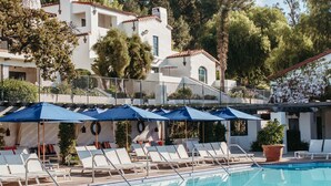 A pool area with lounge chairs and umbrellas, surrounded by a white building with multiple windows and balconies.