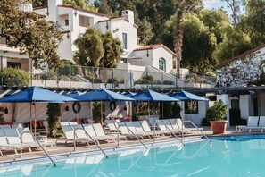 A pool area with lounge chairs and umbrellas, surrounded by a white building with multiple windows and balconies.