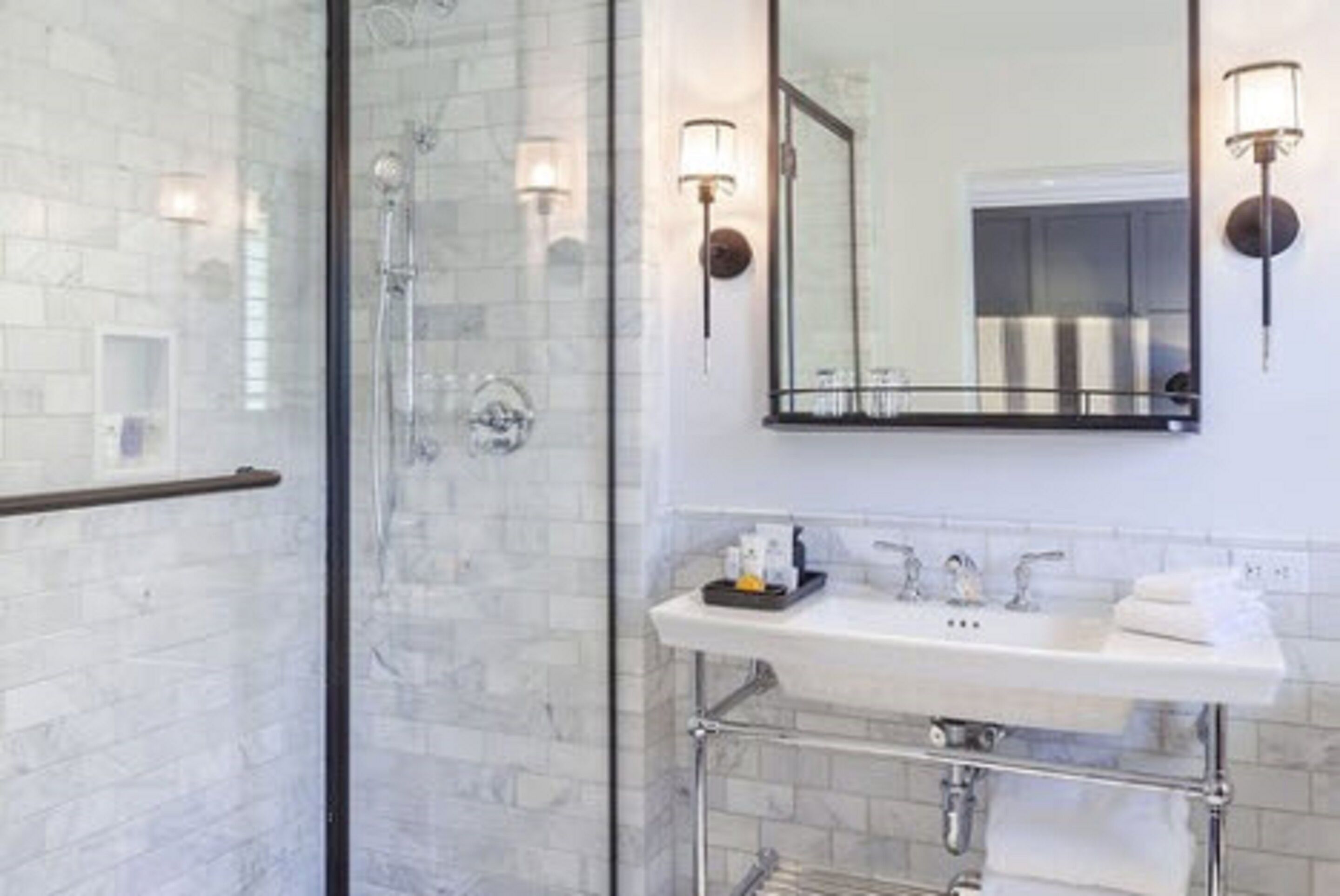Un baño moderno con ducha de vidrio, lavamanos blanco con accesorios cromados y apliques de pared.