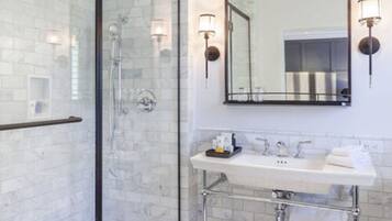 Un baño moderno con ducha de vidrio, lavamanos blanco con accesorios cromados y apliques de pared.