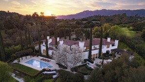 A large, white, two-story house with a swimming pool, surrounded by trees and mountains.