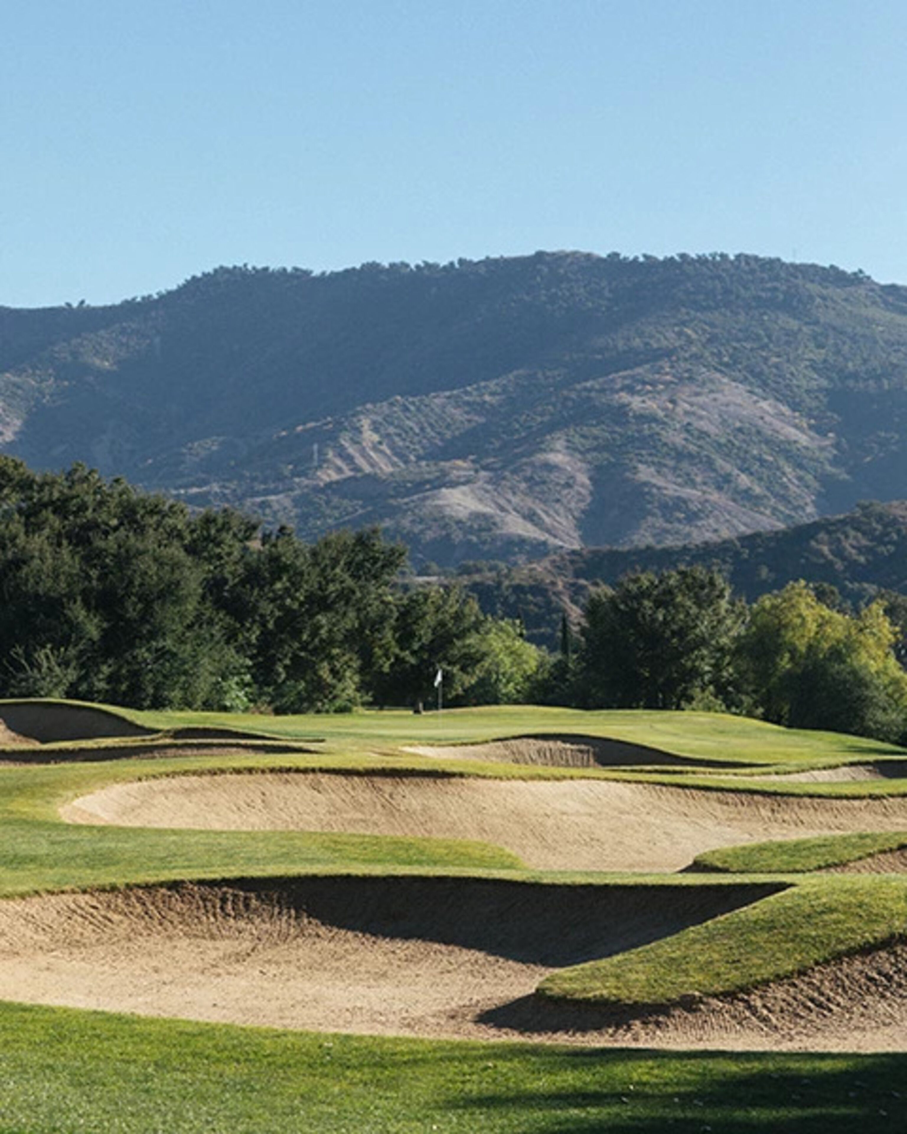 A golf course with sand bunkers and a mountainous backdrop.