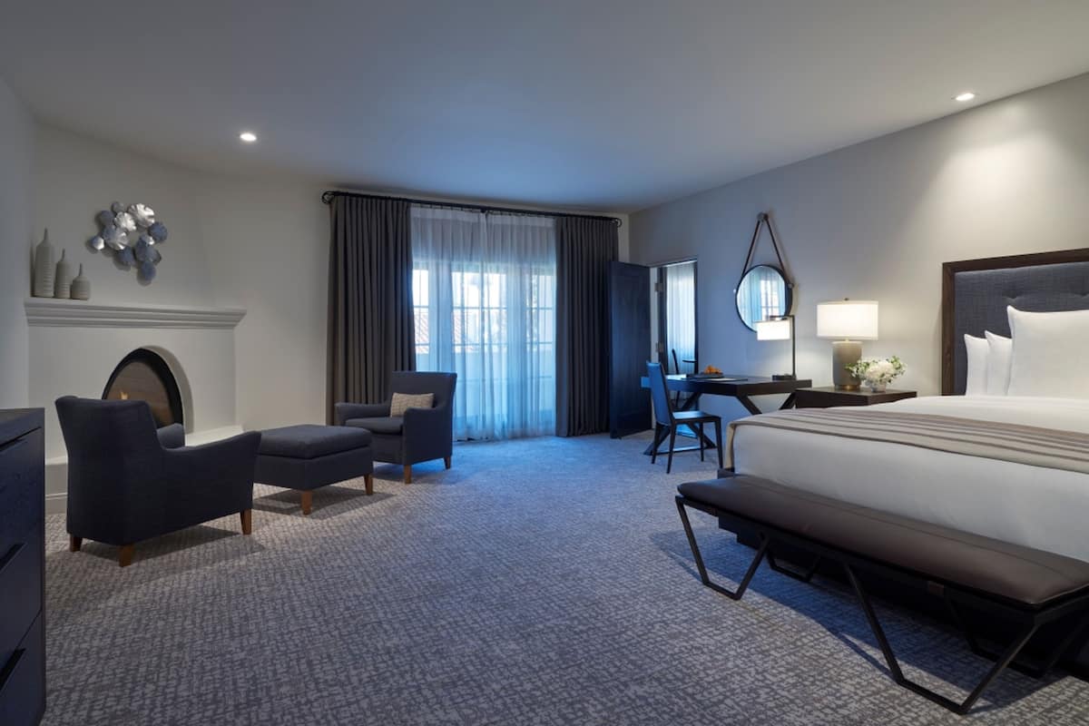 Une chambre d’hôtel avec un grand lit, un bureau, une chaise, un banc et une cheminée.