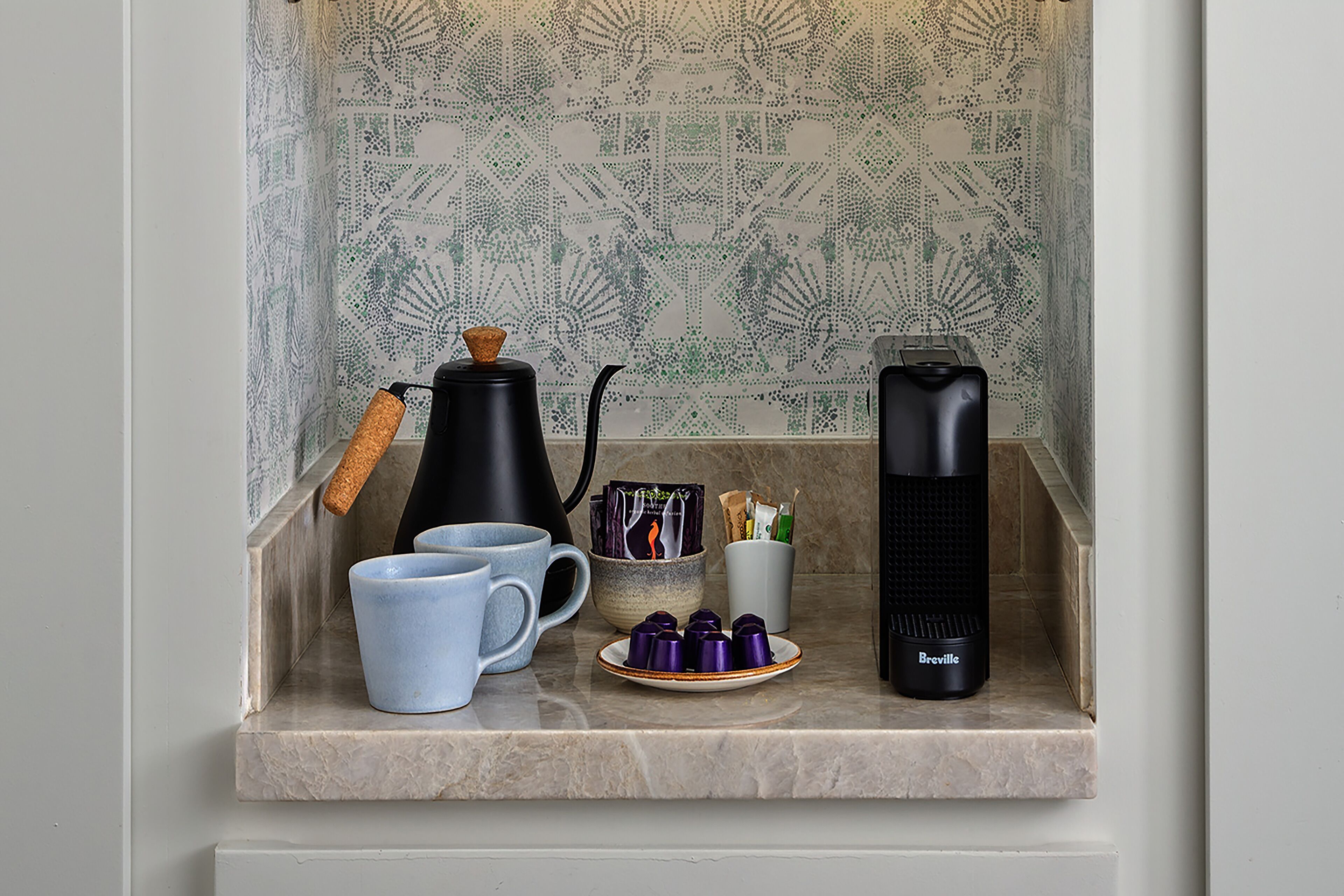 Una encimera de cocina con una cafetera, tazas, un plato con salsas y un aparato Breville.