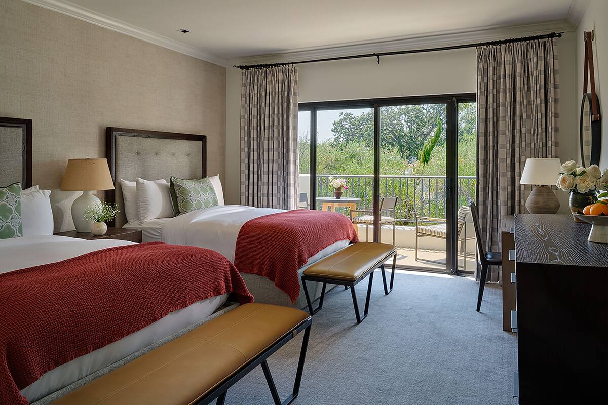Une chambre d’hôtel avec deux lits, une banquette, un bureau et un balcon avec vue.