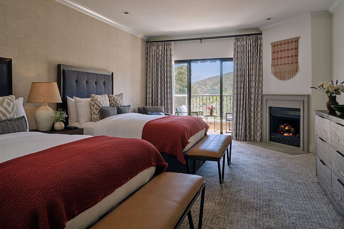 Une chambre d’hôtel avec deux lits, une cheminée, un balcon avec des rideaux et une vue sur l’extérieur.