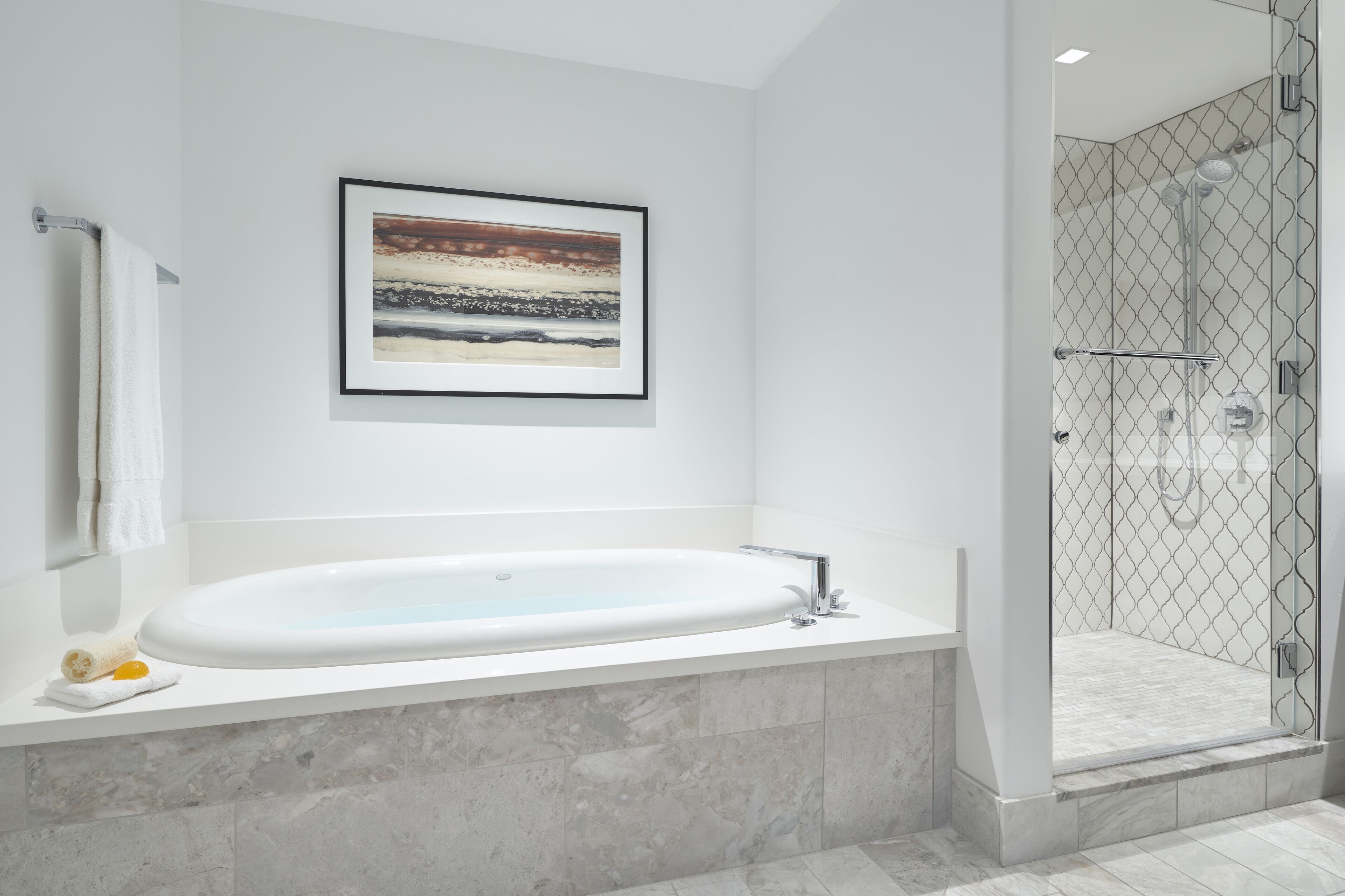 Une salle de bain moderne avec une grande baignoire, une œuvre d’art encadrée au-dessus de la baignoire et un espace douche fermé par des parois de verre.