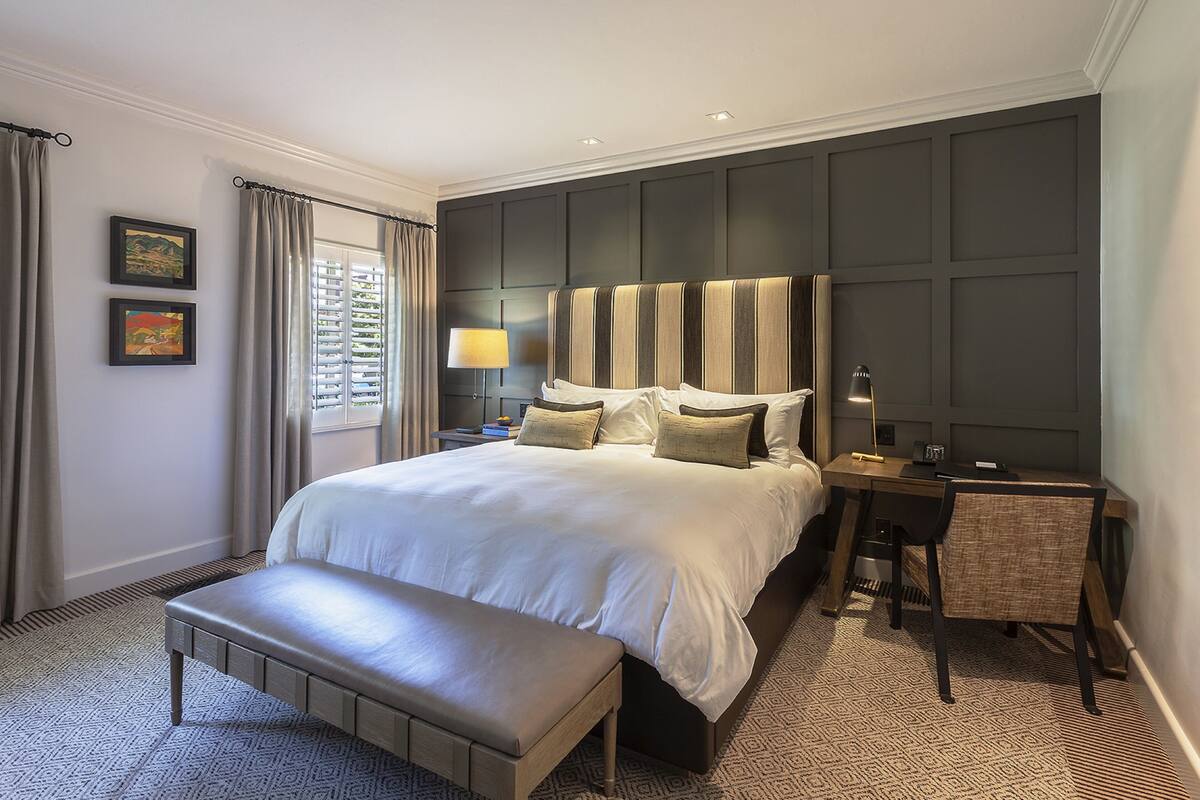 Une chambre bien rangée, avec un grand lit, une table de chevet, un bureau et un banc.