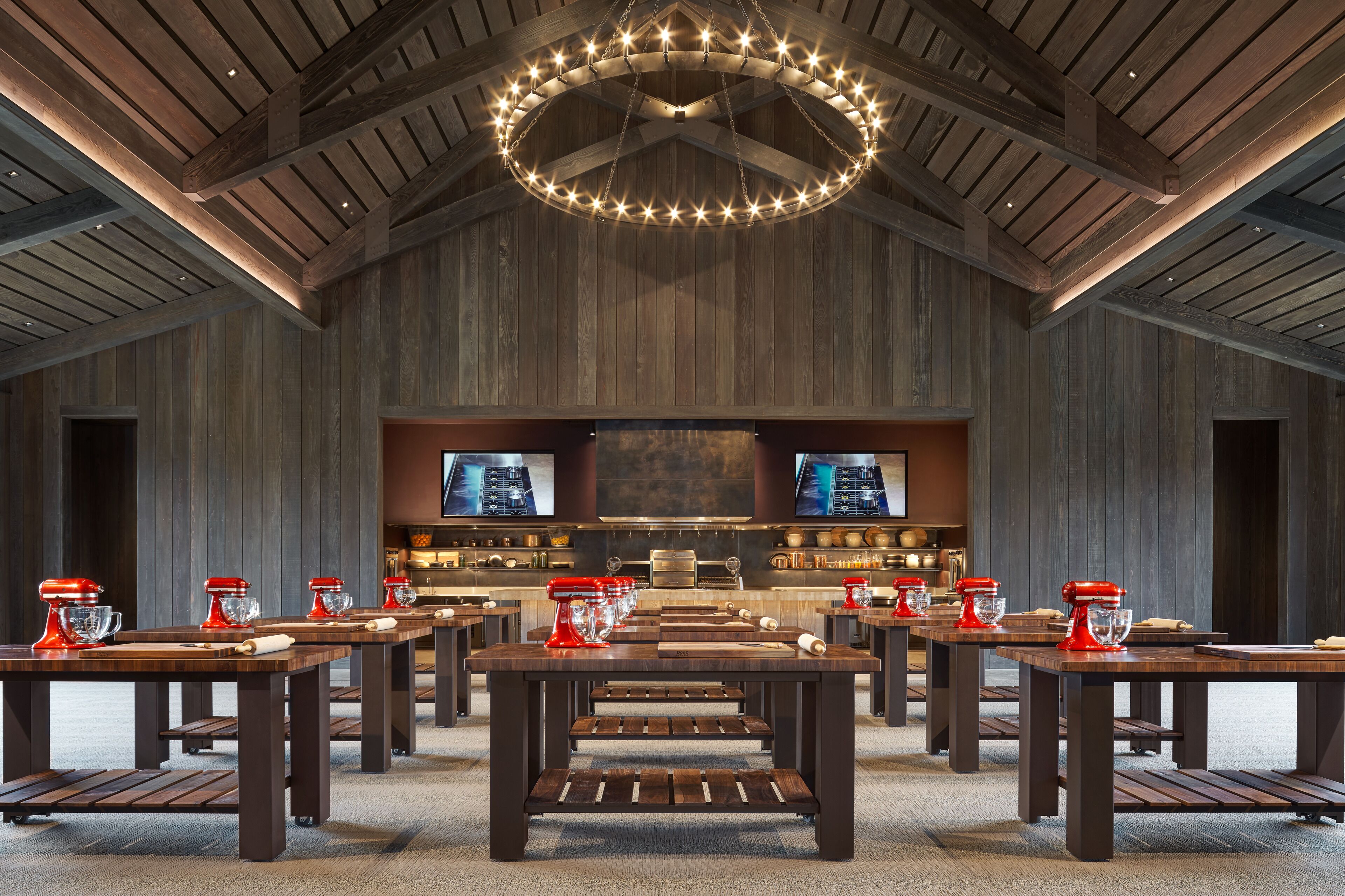 Une cuisine spacieuse, dotée d’appareils électroménagers modernes, de tables en bois et d’un grand luminaire suspendu au plafond.