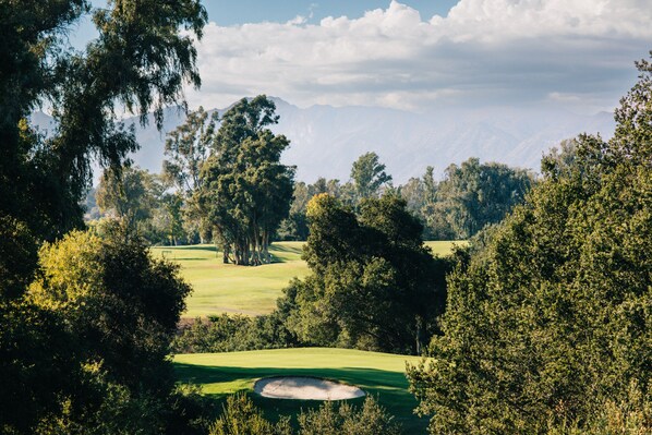 Un parcours de golf avec un bunker de sable, entouré d’une forêt dense et avec une montagne en arrière-plan.