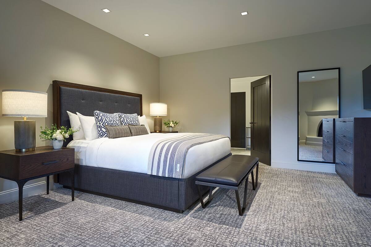 Une chambre d’hôtel moderne avec un grand lit, des tables de chevet, un banc, une commode et un miroir.