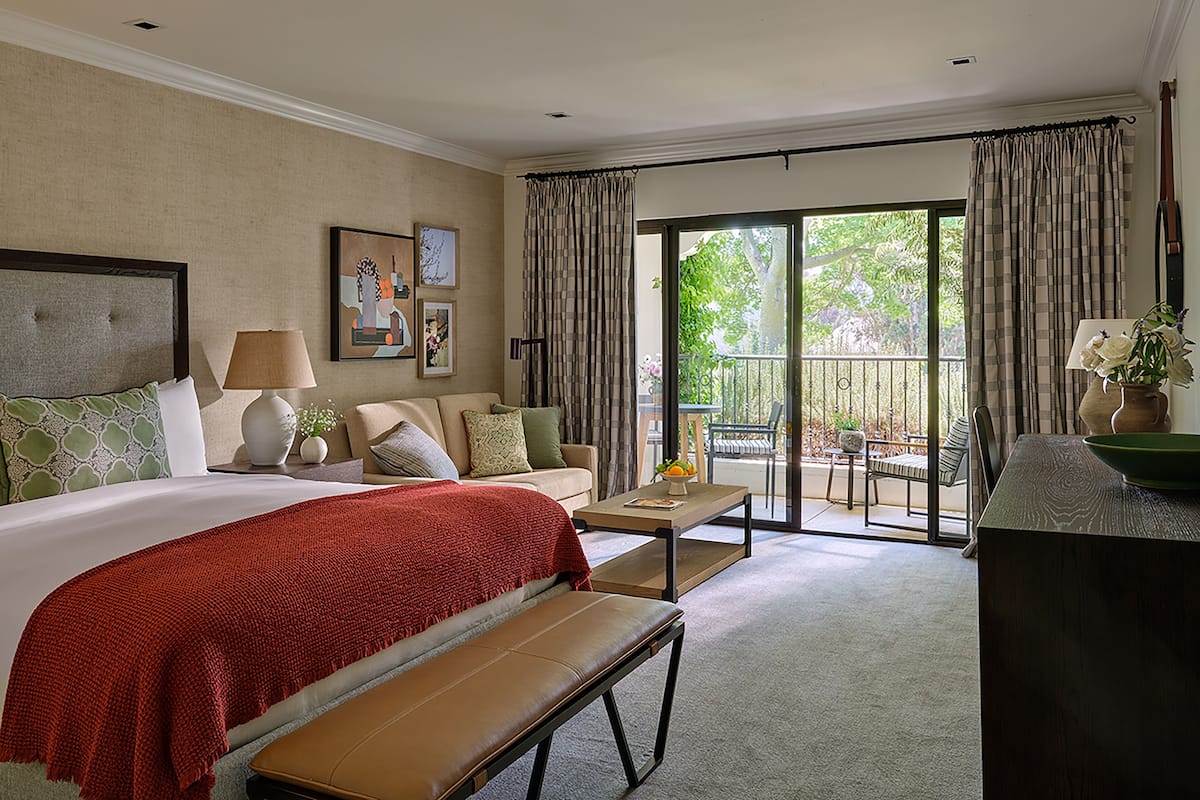 Une chambre d’hôtel dotée d’un grand lit, d’une banquette, d’un canapé, d’une table basse et d’un balcon offrant une vue sur l’extérieur.