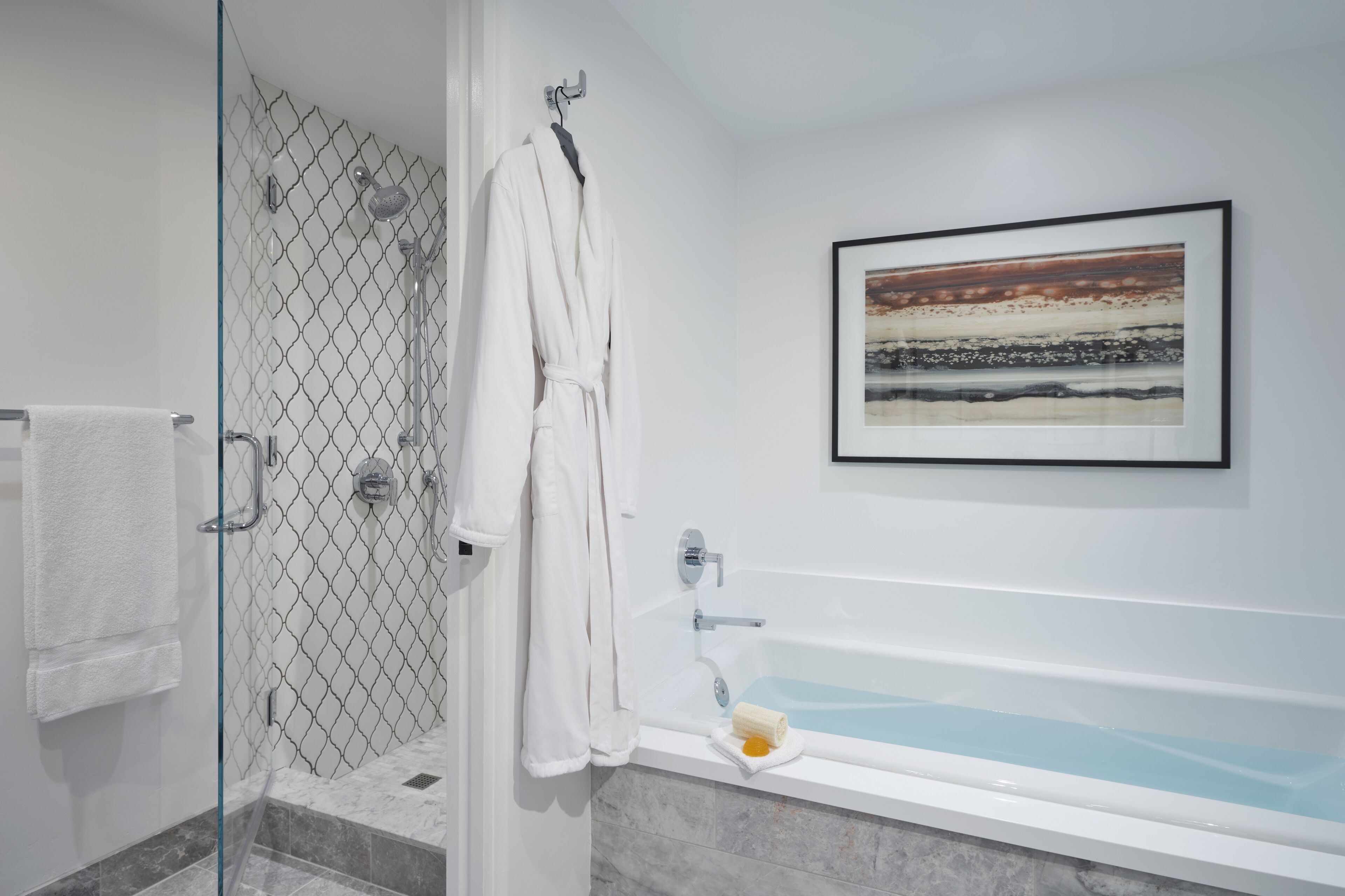 A modern bathroom with a glass-enclosed shower, a white bathtub, and a framed artwork on the wall.