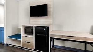 Una kitchenette compacta con microondas integrado, un refrigerador negro y una encimera de madera.