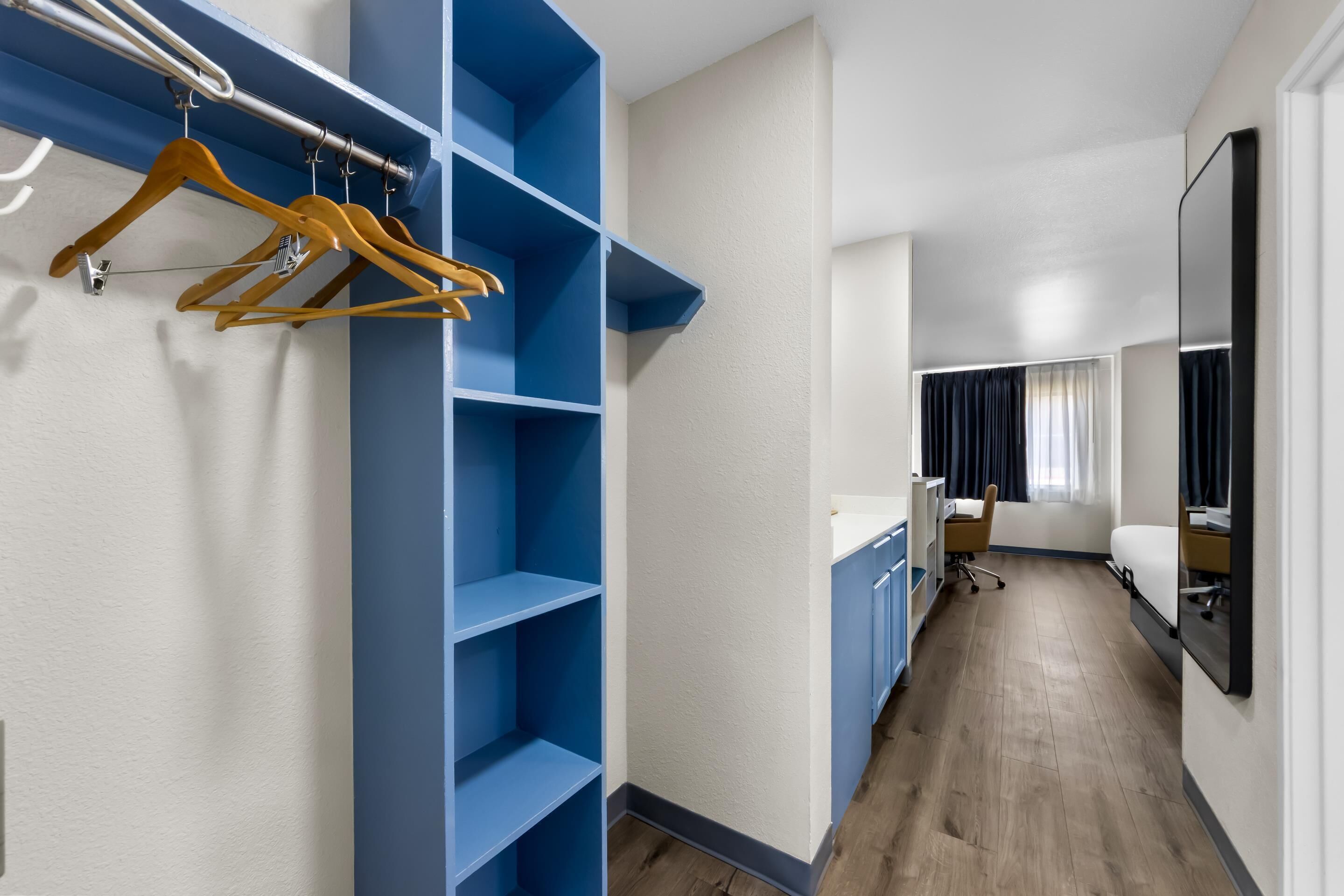 A hotel room with a walk-in closet, a desk, a chair, and a bed.