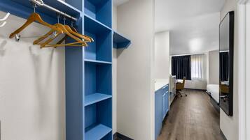 A hotel room with a walk-in closet, a desk, a chair, and a bed.