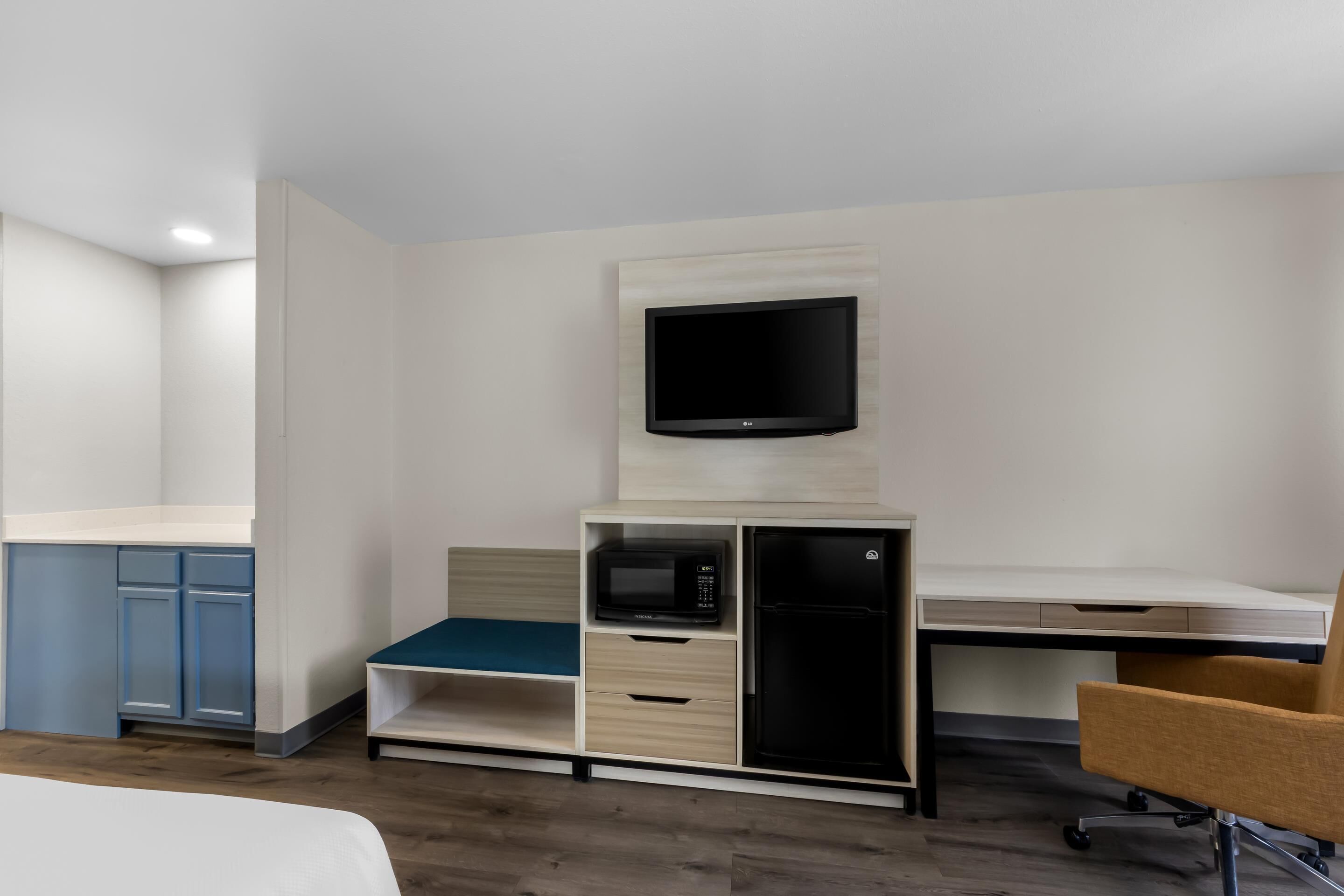 A compact hotel room with a bed, a desk, a television, a microwave, and a refrigerator.